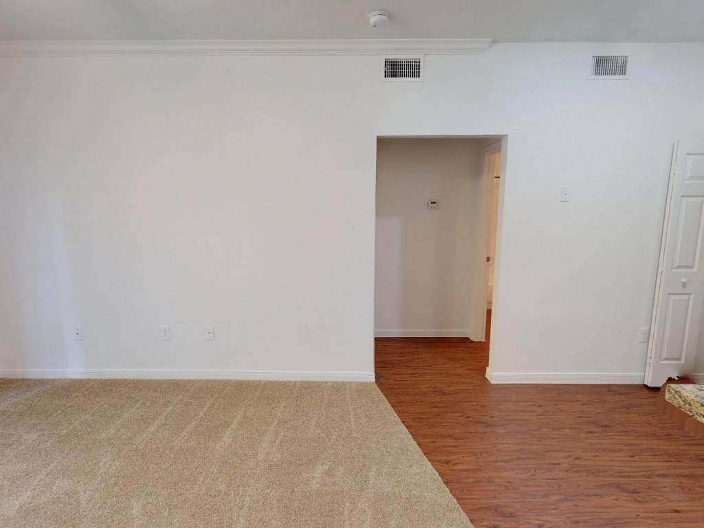 A room with a carpet and wooden flooring with a doorway leading to another room.