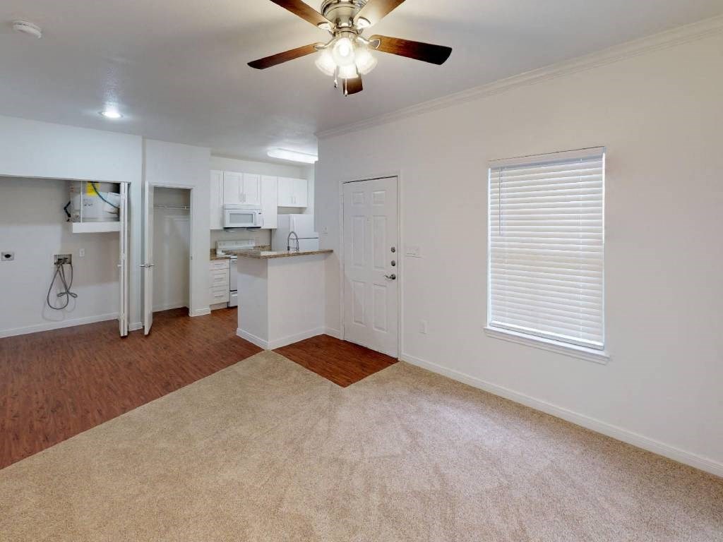 A room with a ceiling fan and a kitchen area in the background.