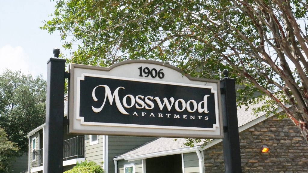 A sign for Mosswood Apartments is displayed in front of a building.