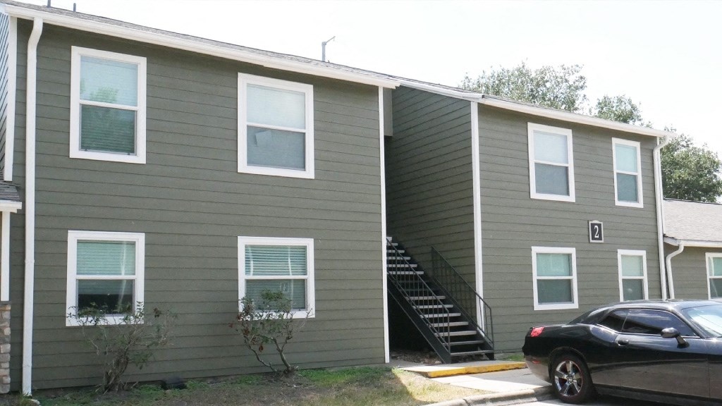 A black car is parked in front of a grey building with a staircase leading to the entrance.