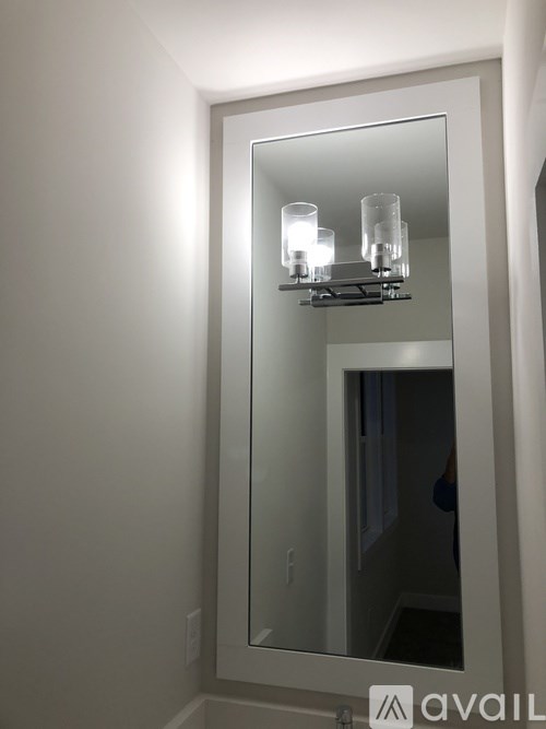 A mirror with a light on it reflects a room with a door.