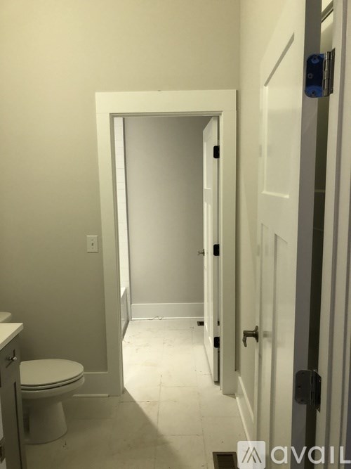 A white toilet is in a small bathroom with a doorway leading to another room.