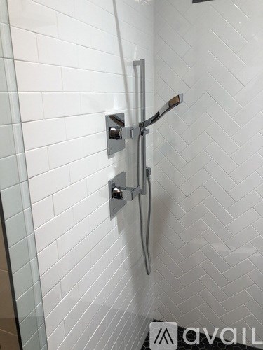 A white tiled shower with a silver shower head and hand held shower.
