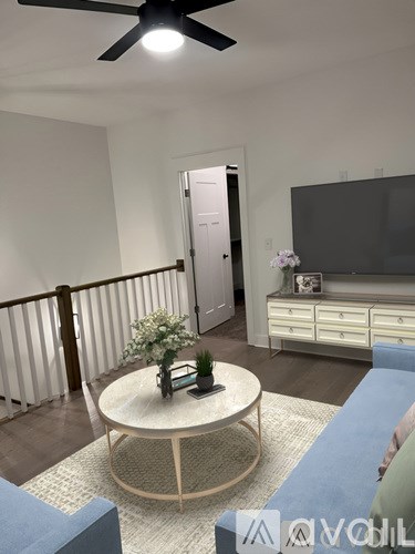 A living room with a white ceiling fan and a round table with a vase of flowers on it.