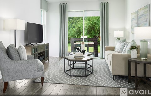 A living room with a grey sofa, a grey armchair, a black television, and a glass table with a vase on it.