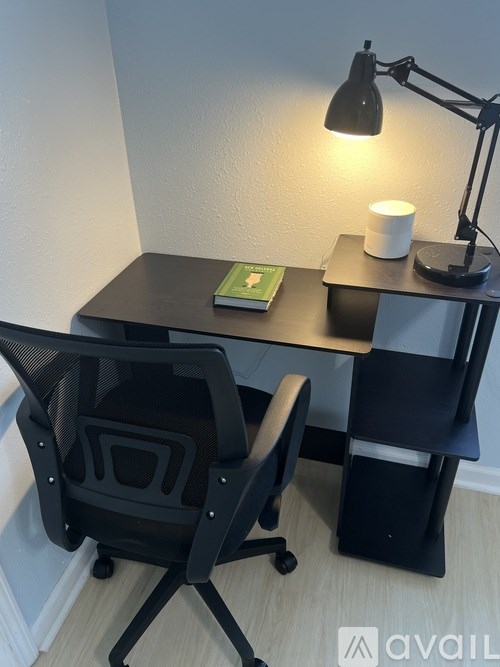 A black desk with a chair, a book, and a lamp.