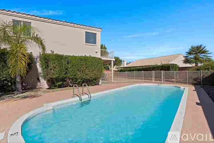 A swimming pool in front of a house with a fence and a tree.