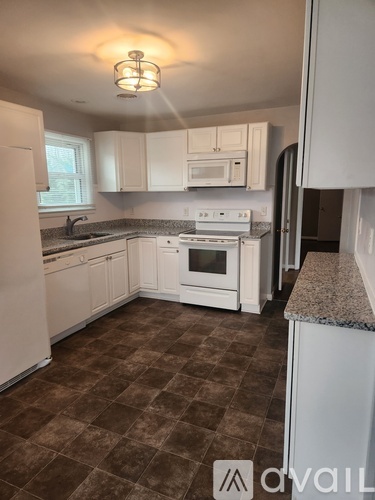 A kitchen with white appliances and brown tiled flooring.