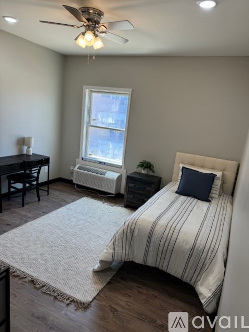 A bedroom with a bed, a desk, and a window.