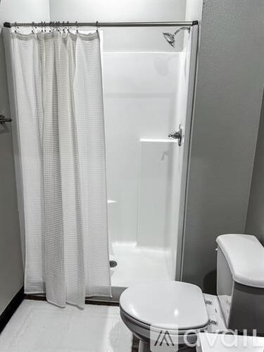 A white toilet sits next to a white shower curtain in a bathroom.