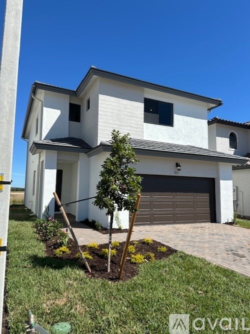 A white house with a brown garage door and a tree in front.