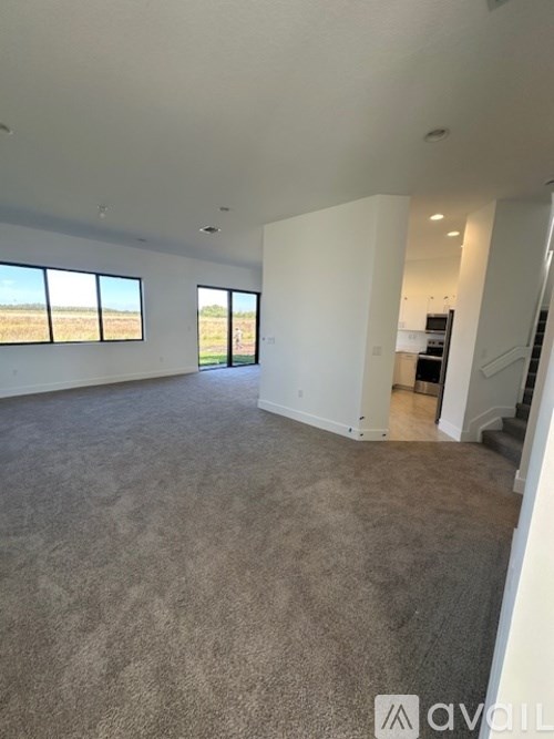 A large, empty room with carpeted flooring and a staircase leading to another level.