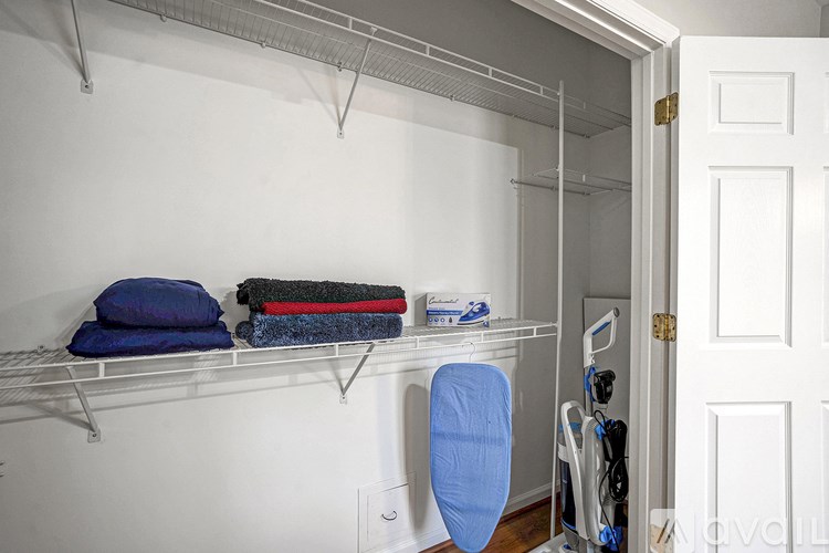 A white closet with a blue chair and some clothes.