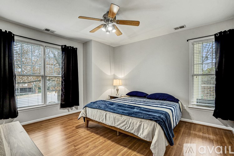 A bedroom with a bed, a ceiling fan, and a window with black curtains.