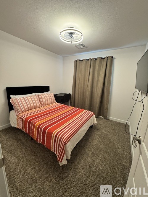 A bedroom with a bed, a television, and a window with curtains.