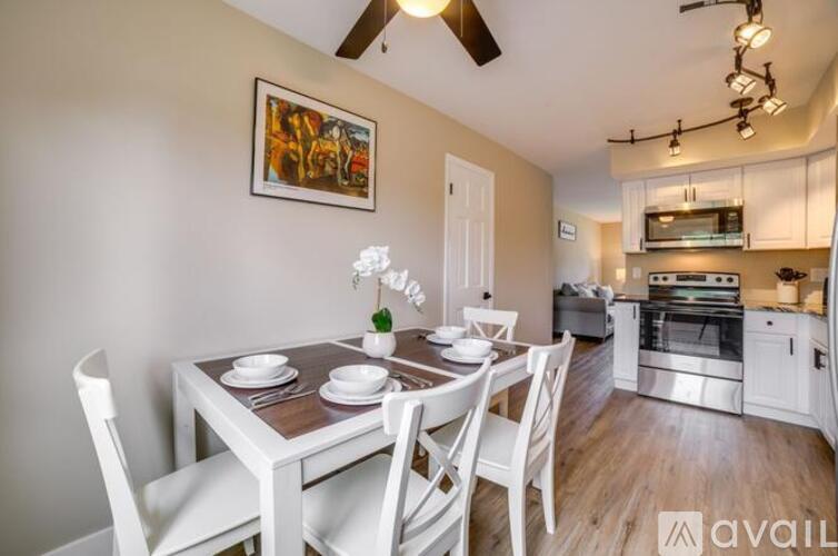 A dining room with a white table and chairs, a ceiling fan, and a painting on the wall.