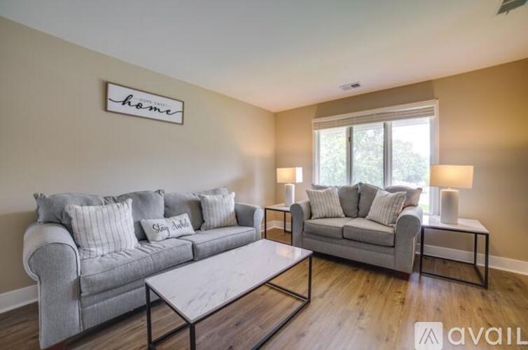 A living room with a grey couch, a white coffee table, and a window with a view of trees.