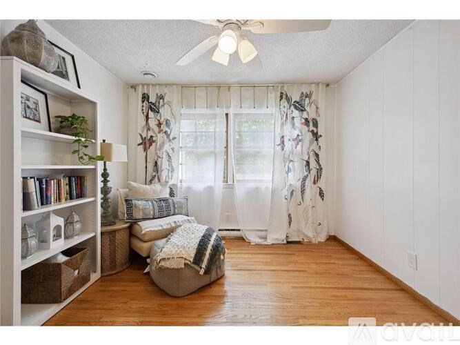 A living room with a bookshelf, a window with curtains, and a ceiling fan.