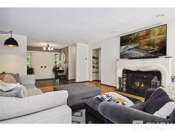 A living room with a grey couch, a grey sofa, a grey rug, a grey coffee table, a grey chair, a grey floor lamp, a grey wall, a grey fireplace, a grey painting, a grey door, a