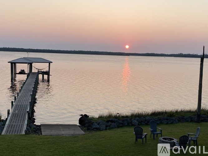 A dock extends into a calm body of water with a sunset in the distance.
