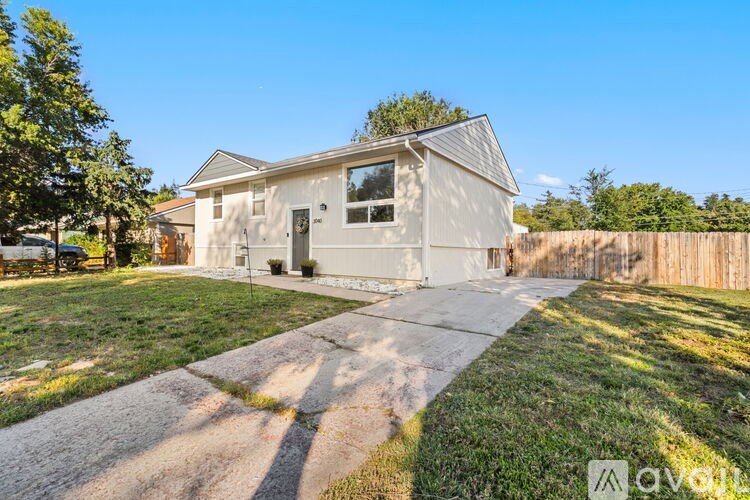 A house with a grey roof and a white exterior is surrounded by a wooden fence and a grassy area.