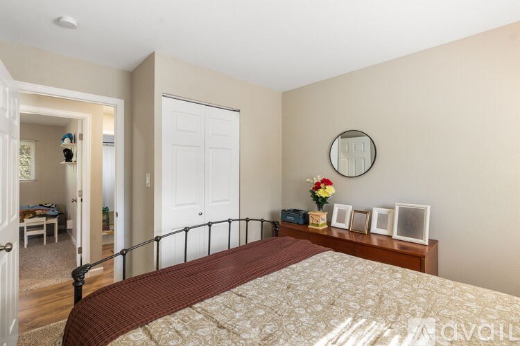 A bedroom with a bed, dresser, mirror, and a small table with a vase of flowers.