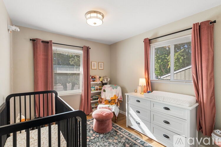 A baby nursery with a crib, changing table, and a window with curtains.