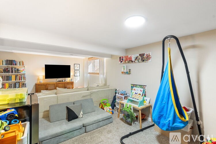 A living room with a grey sofa, a television, a bookshelf, and a hanging blue chair.