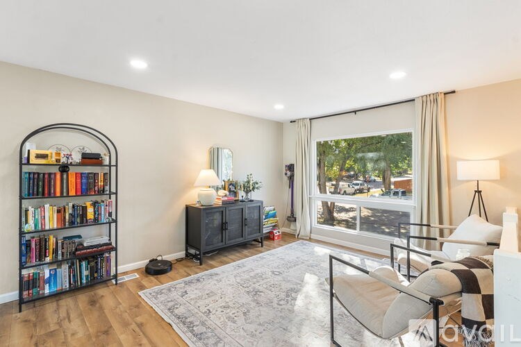 A living room with a bookshelf, a sofa, and a large window.