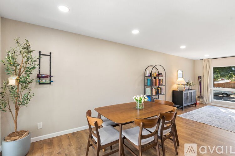 A dining room with a wooden table and chairs, a potted plant, and a bookshelf with books.