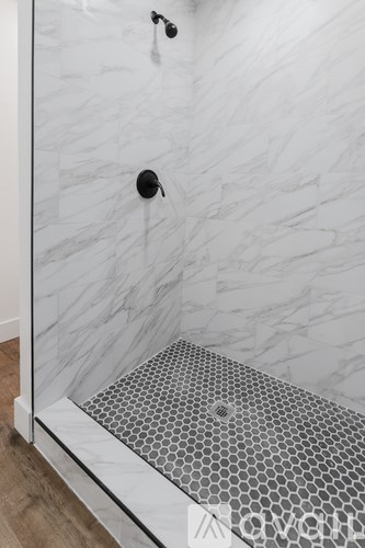 A shower with a marble wall and a hexagonal tile floor.
