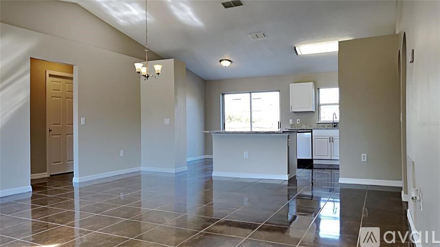 A spacious living room with tile flooring and a kitchen area in the background.
