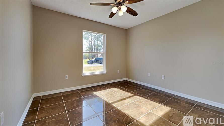 A room with a ceiling fan and a window showing a view of a yard and a car.