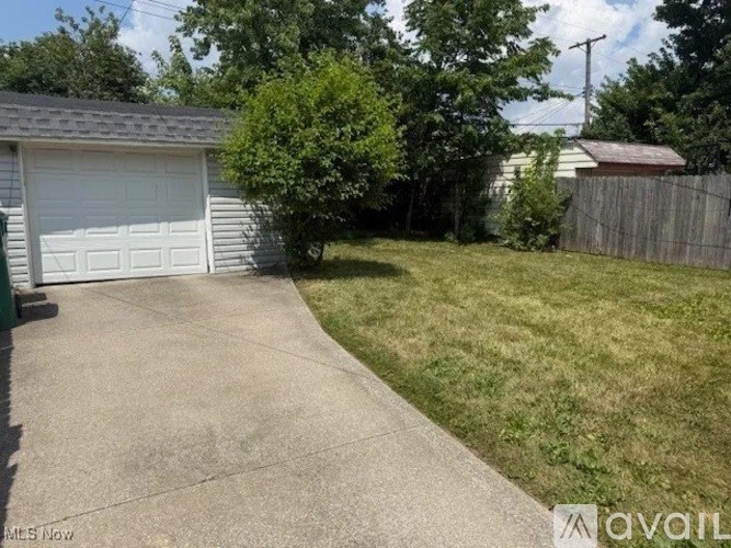 A driveway leads to a garage with a tree and a fence in the background.