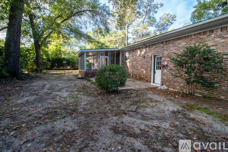 A small house with a white door is surrounded by trees and has a gravel driveway.