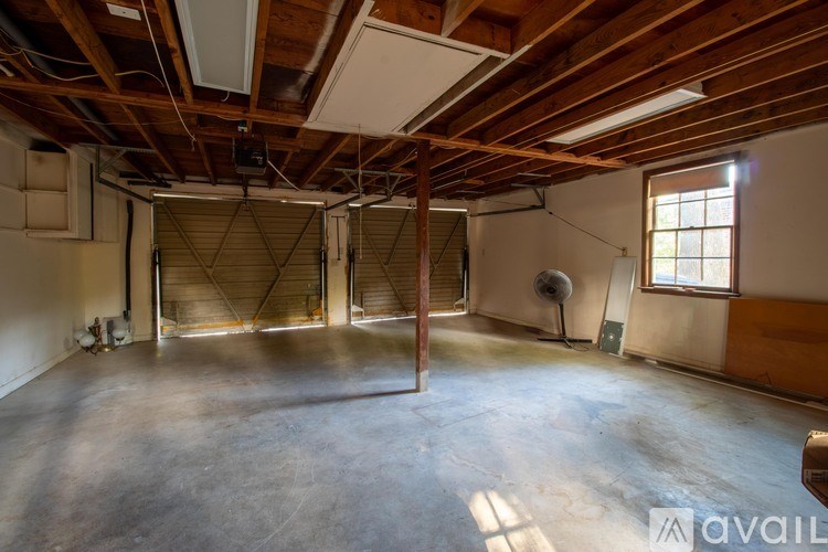 A large empty room with wooden beams on the ceiling and a fan on the wall.