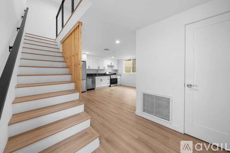 A wooden staircase with a black railing leads to a brightly lit kitchen area.