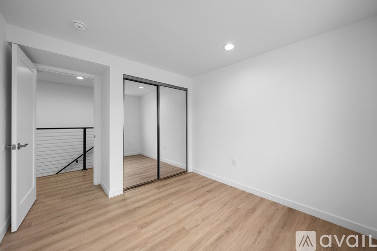 A room with a white wall and wooden floor with a door and a mirror.