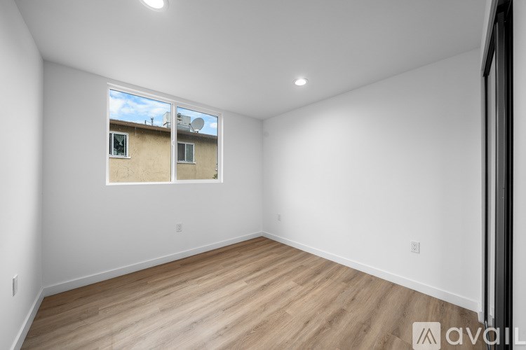A spacious empty room with wooden flooring and a window showing a view of a building outside.