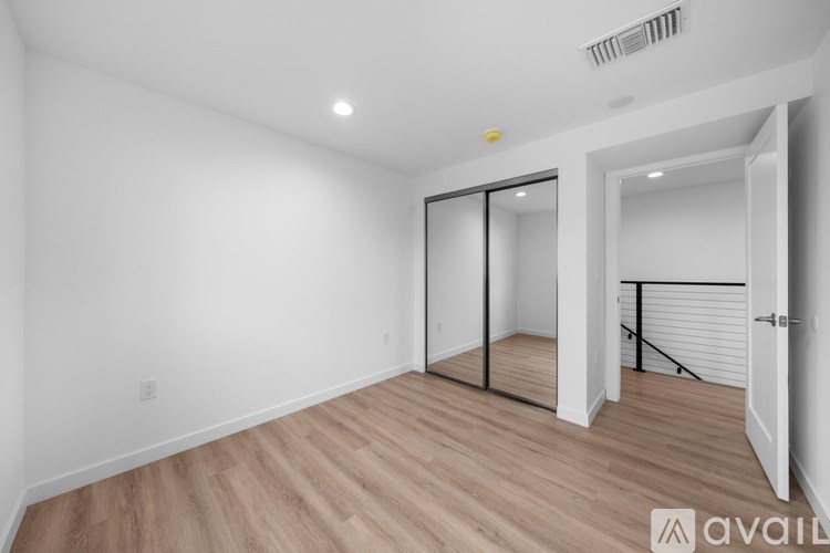 A room with wooden flooring and white walls, with a door on the right and a window on the left.
