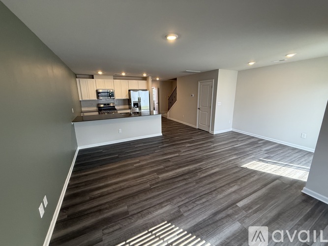 A spacious room with wooden flooring and a kitchen area in the background.