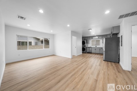 A spacious room with wooden flooring and a kitchen area in the background.
