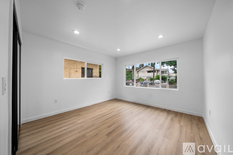 A spacious room with wooden flooring and a large window showing a view of a house.