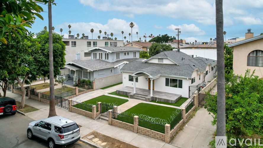 A house with a grey roof is surrounded by a fence and has a car parked in front.