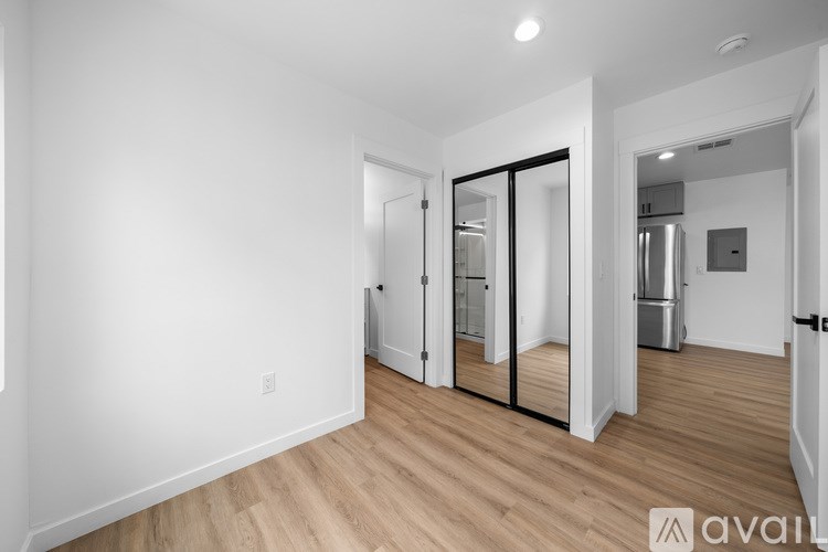 A spacious room with wooden flooring and white walls, featuring a kitchen area with a refrigerator, a sink, and a stove.