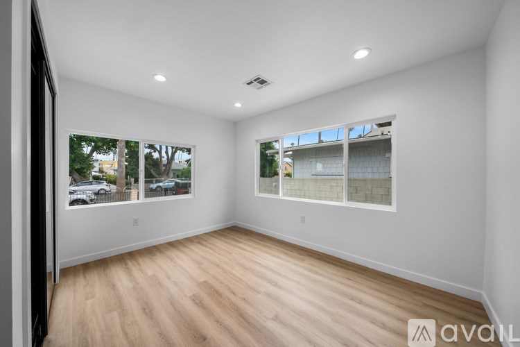 A spacious room with wooden flooring and two windows.