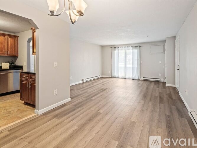 A spacious living room with hardwood floors and a kitchen area to the left.