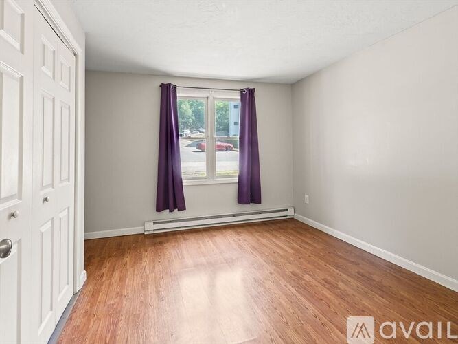 A room with a wooden floor and a window with purple curtains.