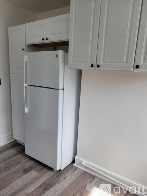 A white refrigerator in a kitchen with white cabinets.