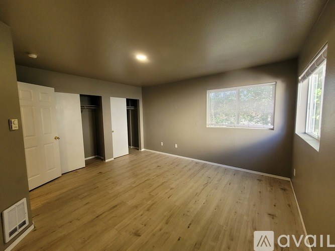 A room with wooden flooring and a window showing greenery outside.